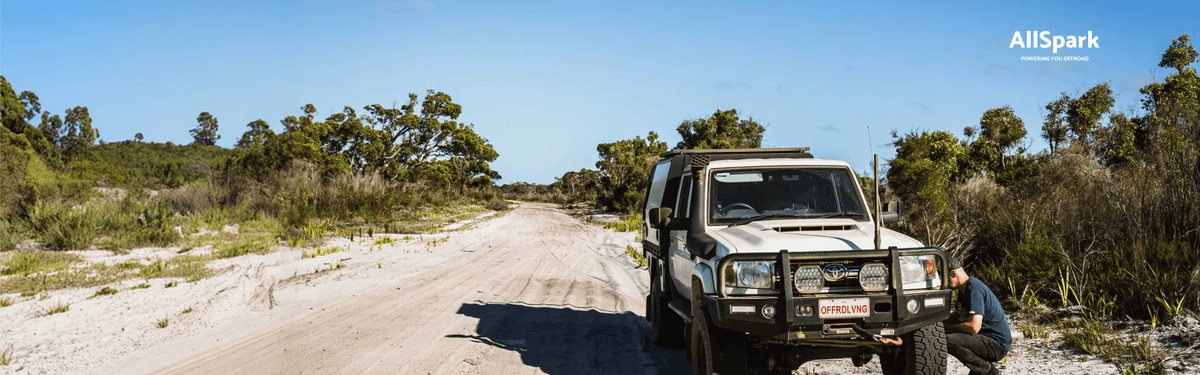 Toyota LandCruiser parked on a sandy bush track while its driver checks the wheel